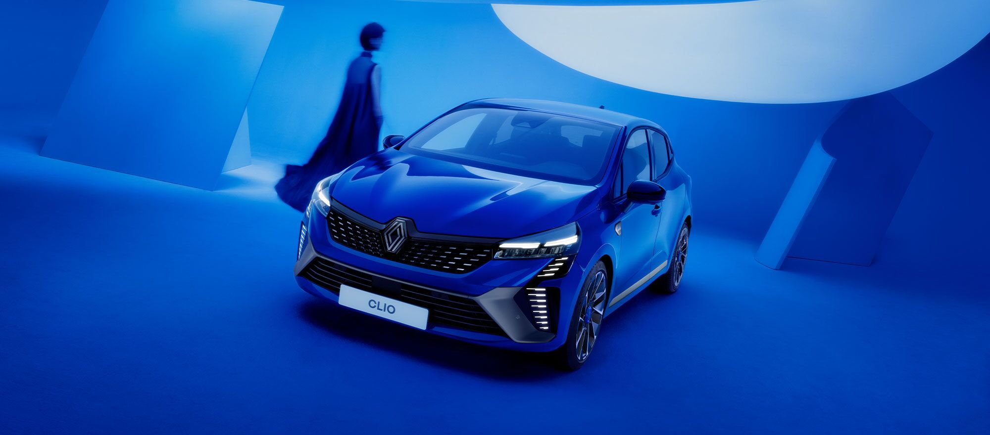 Eine Frau im blauen Kleid läuft an einem blauen Renault Clio vorbei