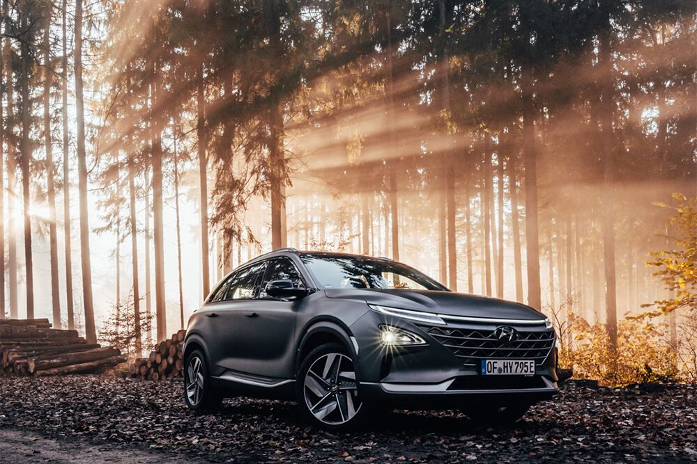 Ein Hyundai NEXO parkt im Wald und im Hintergrund scheint die Sonne durch den Wald