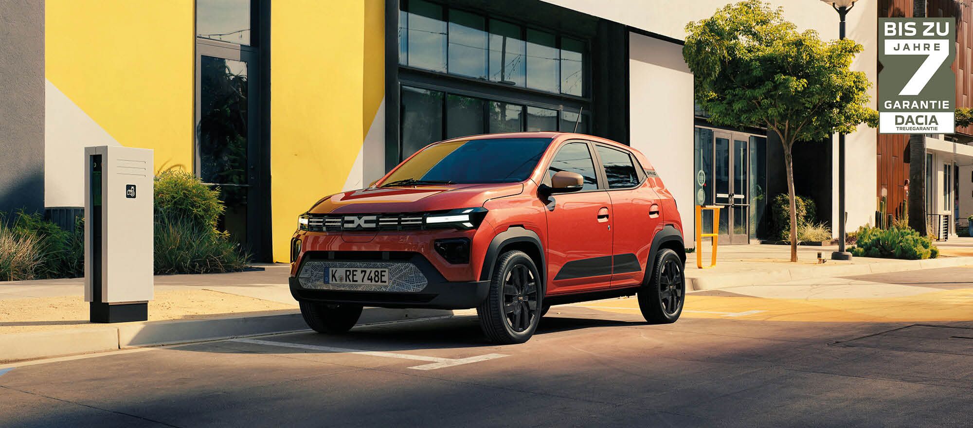 Der Dacia Spring steht auf einem Parkplatz vor einer Elektroladesäule