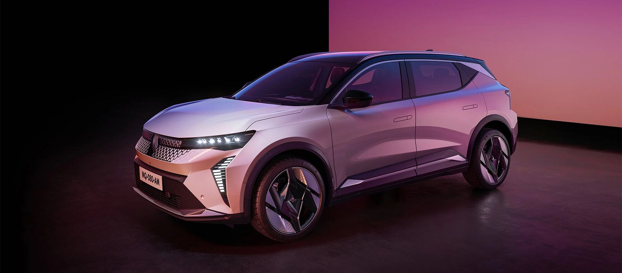 Der Renault Scenic E-Tech mit leuchtenden Lichtern vor einer lilafarbenen Wand