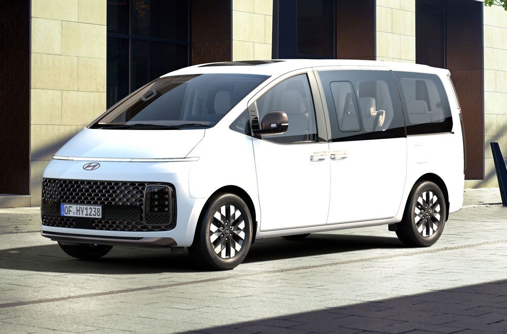 Ein weißer Hyundai Staria im Seitenprofil steht vor einer Steinfront eines Ladengeschäfts