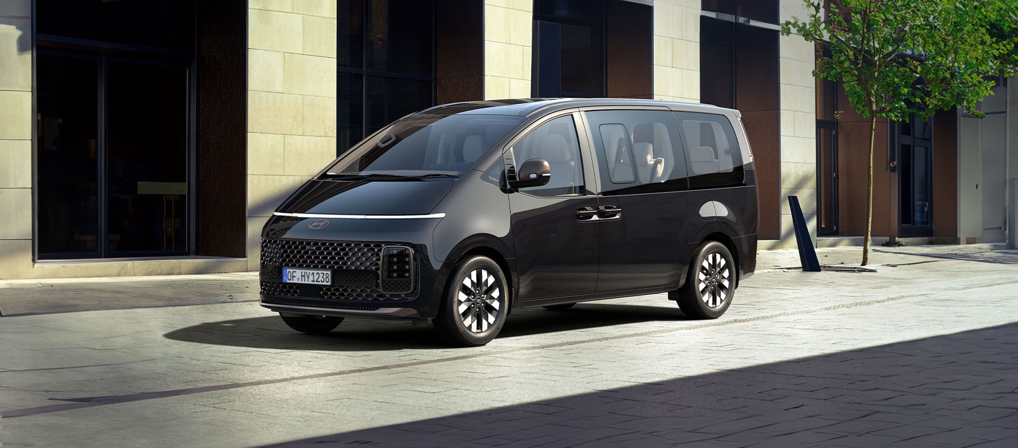 Schwarze Hyundai STARIA vor einem Baum und einer Ladenzeile