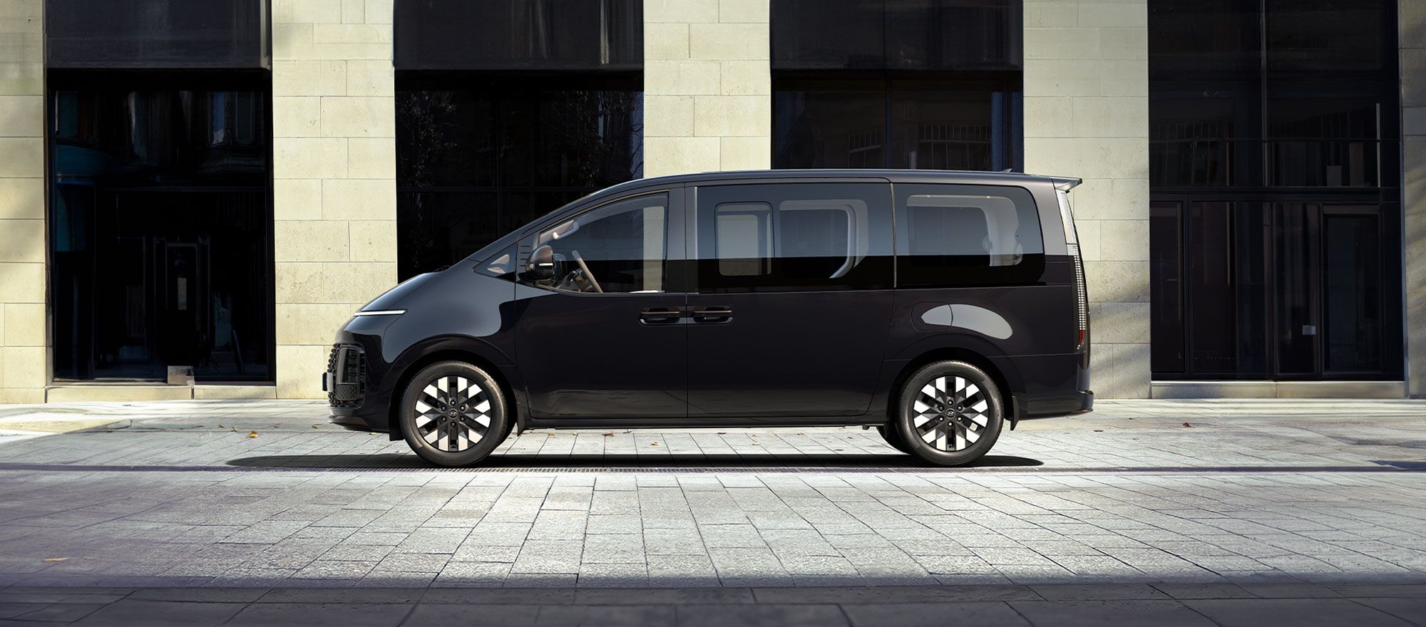 Seitenprofil eines schwarzen Hyundai STARIA vor einer Steinfront