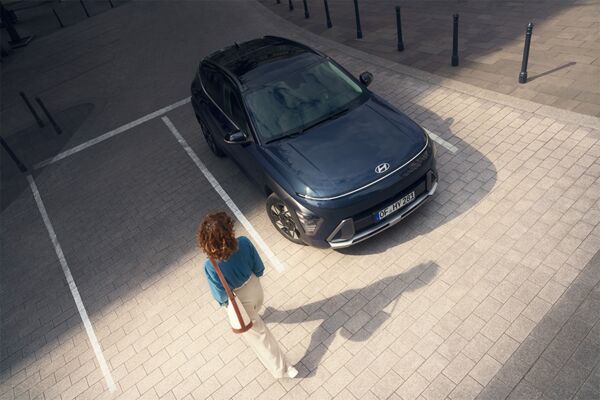 Ein parkender Hyundai KONA auf den eine Frau zuläuft