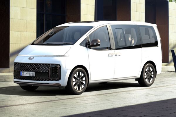 Ein weißer Hyundai Staria im Seitenprofil steht vor einer Steinfront eines Ladengeschäfts