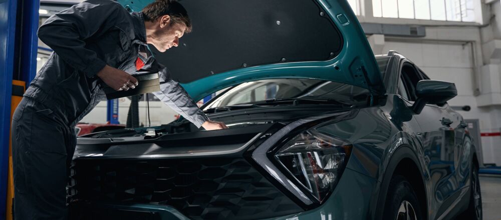 Ein KFZ Mechaniker leuchtet den offenen Motor eines Kia Fahrzeugs ab
