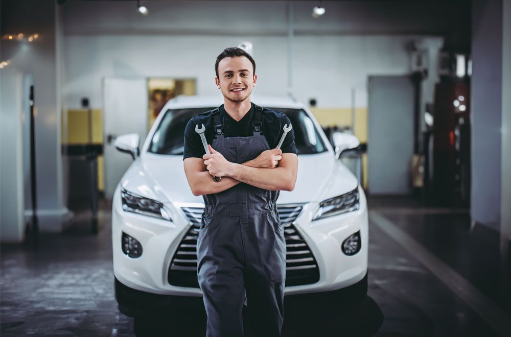 Ein KFZ Mechaniker in der Werkstatt vor einem Auto mit seinem Werkzeug in der Hand