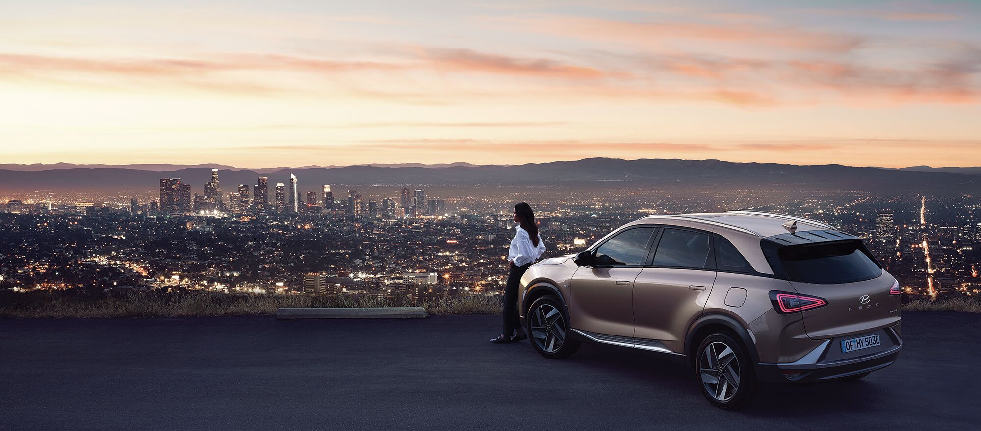 Frau lehnt an Hyundai NEXO an und schaut auf eine Stadt Skyline