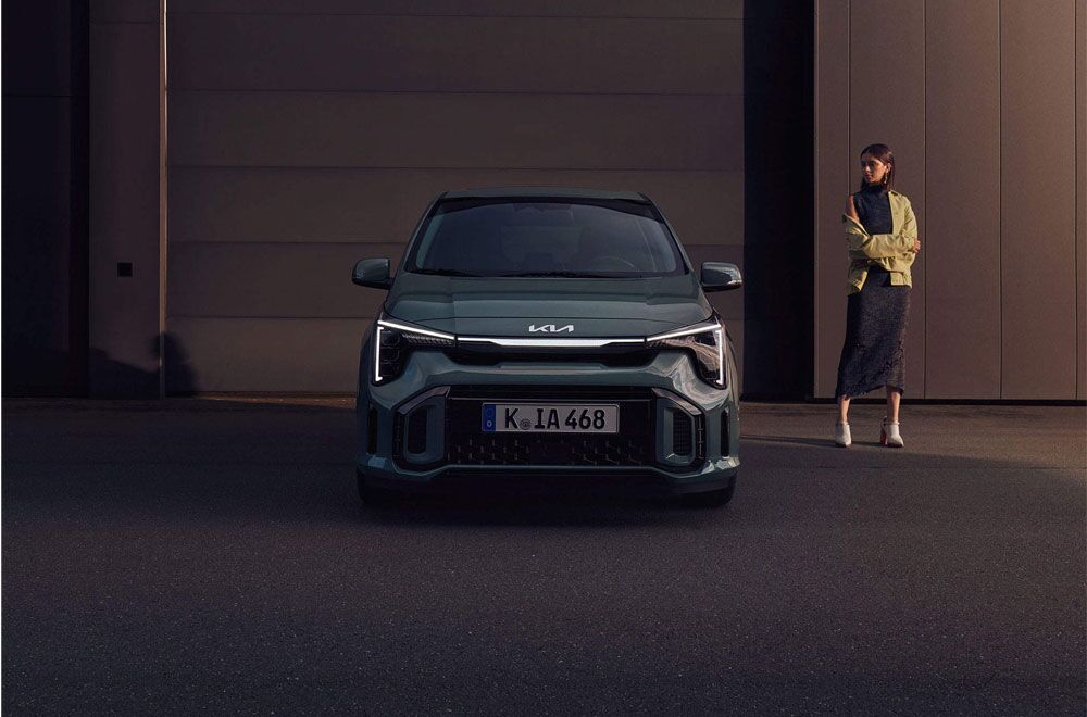 Die Front und Lichtsignatur des Kia Picanto neben dem eine Frau steht